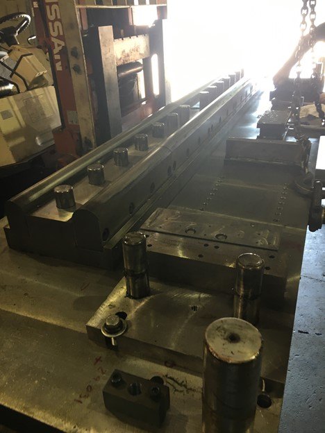 A long stamping die in a press, with guide posts in the foreground
