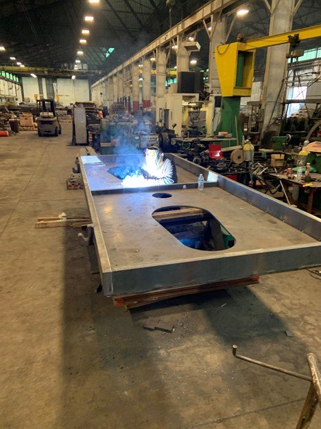 A welder working on a large steel frame in the main bay of the plant